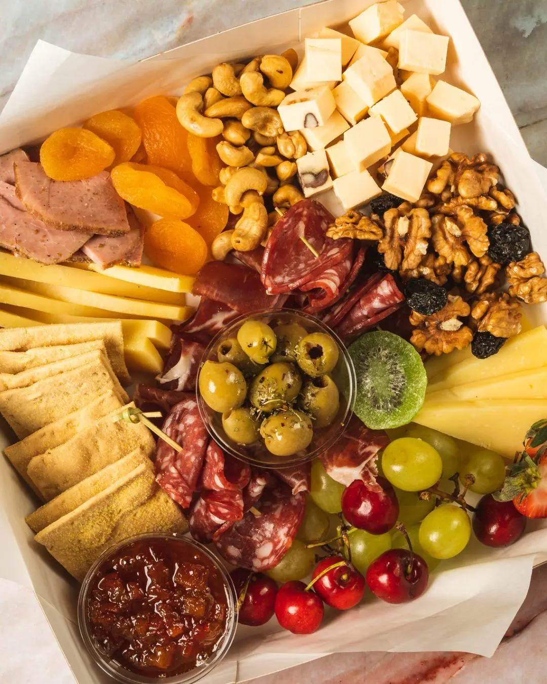 A catering box of cured meats, cheeses, crackers and fresh fruit