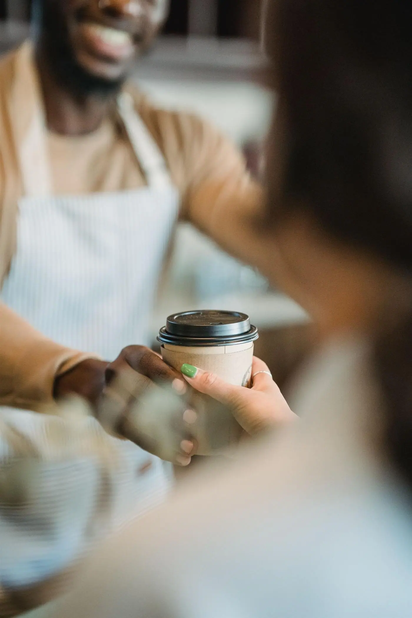 A café worker passing a takeaway coffee cup to a customer across the counter