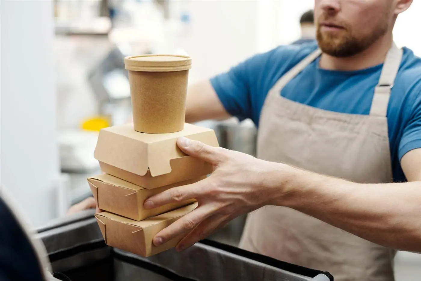 A worker carrying stacked kraft takeaway boxes and a soup container