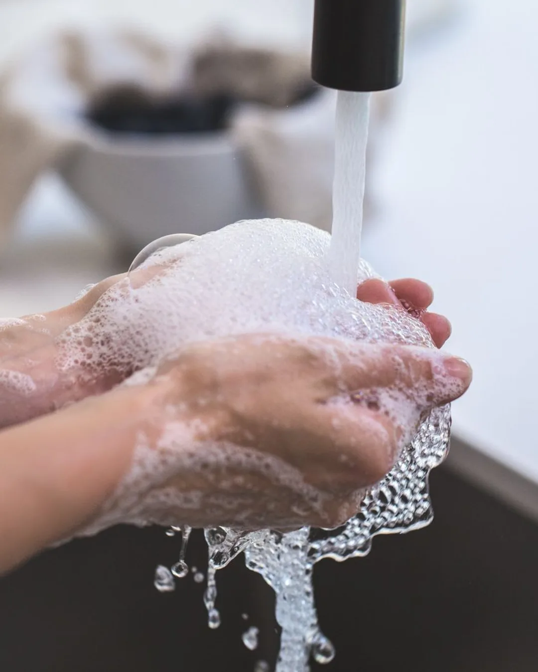 Hands being washed with foamy soap under a tap